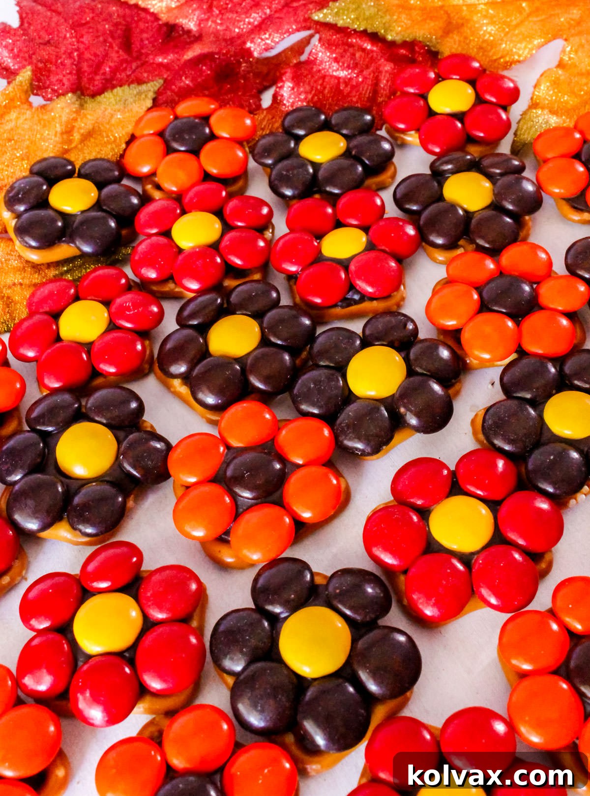 A closeup of a beautiful batch of Harvest Flower Pretzel Bites artfully arranged on a white table, surrounded by rustic Fall decorations, showcasing their vibrant colors and appealing textures.