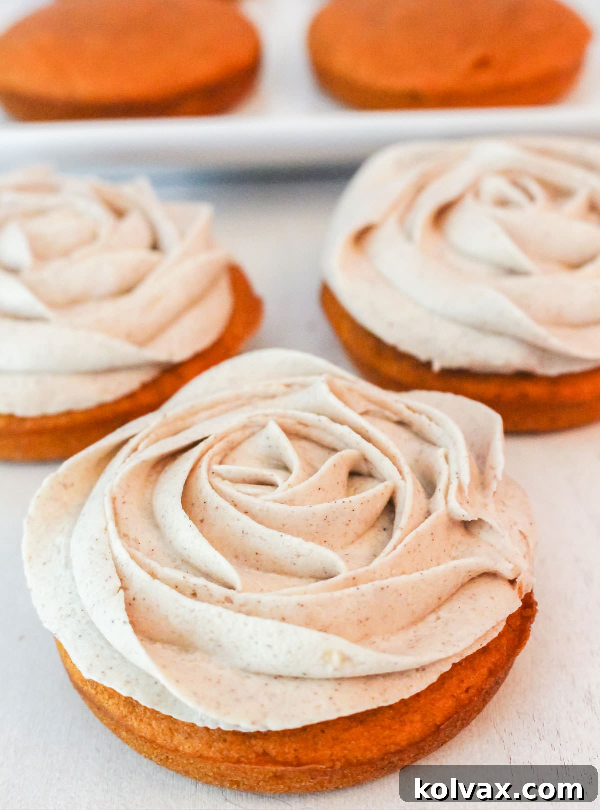 A trio of beautifully frosted Pumpkin Mini Cakes with cinnamon buttercream, perfectly arranged on a minimalist white table, awaiting enjoyment.