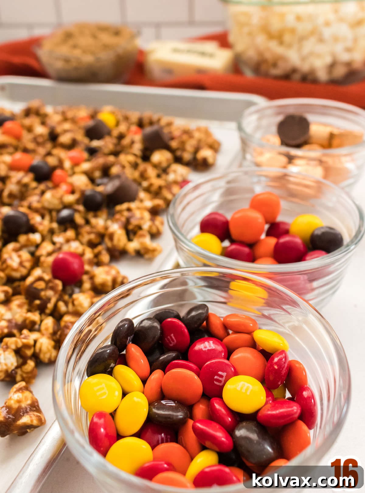 Closeup on three glass ramekins filled with M&M's Pretzel M&M's and Rolo Candies sitting next to a cookie sheet filled with Harvest Caramel Corn.