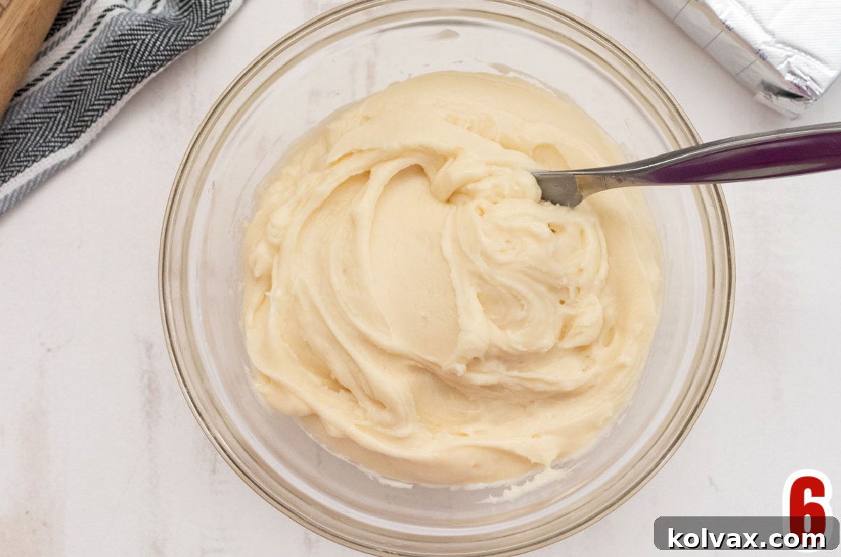 Close-up of a glass mixing bowl filled with homemade Cream Cheese Frosting, ready to be spread onto the cooled apple bread.
