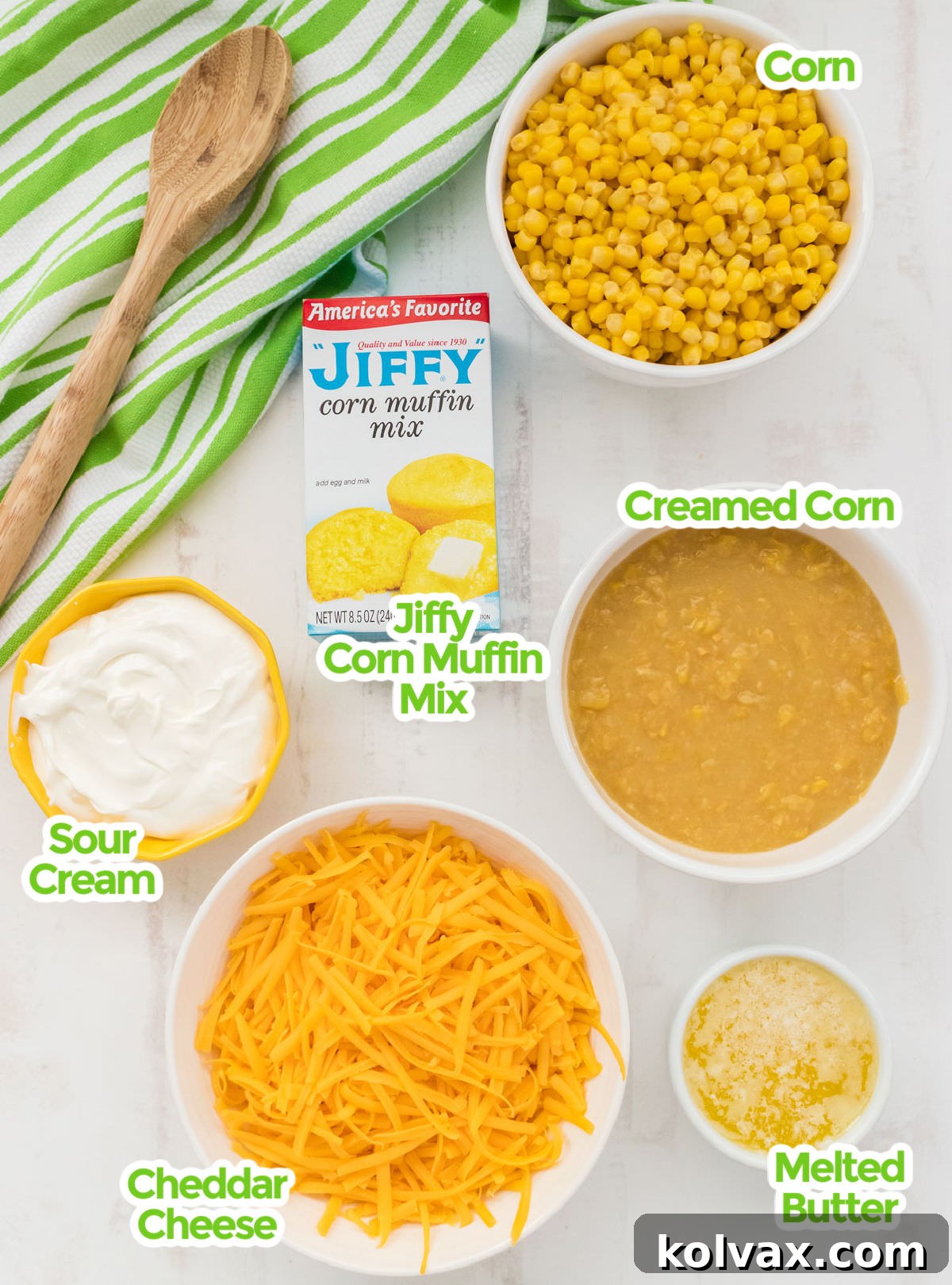All the ingredients you will need to make Corn Casserole including Canned Corn, Creamed Corn, Jiffy Corn Muffin Mix, Sour Cream, Melted Butter and Grated Cheddar Cheese, laid out on a wooden surface.