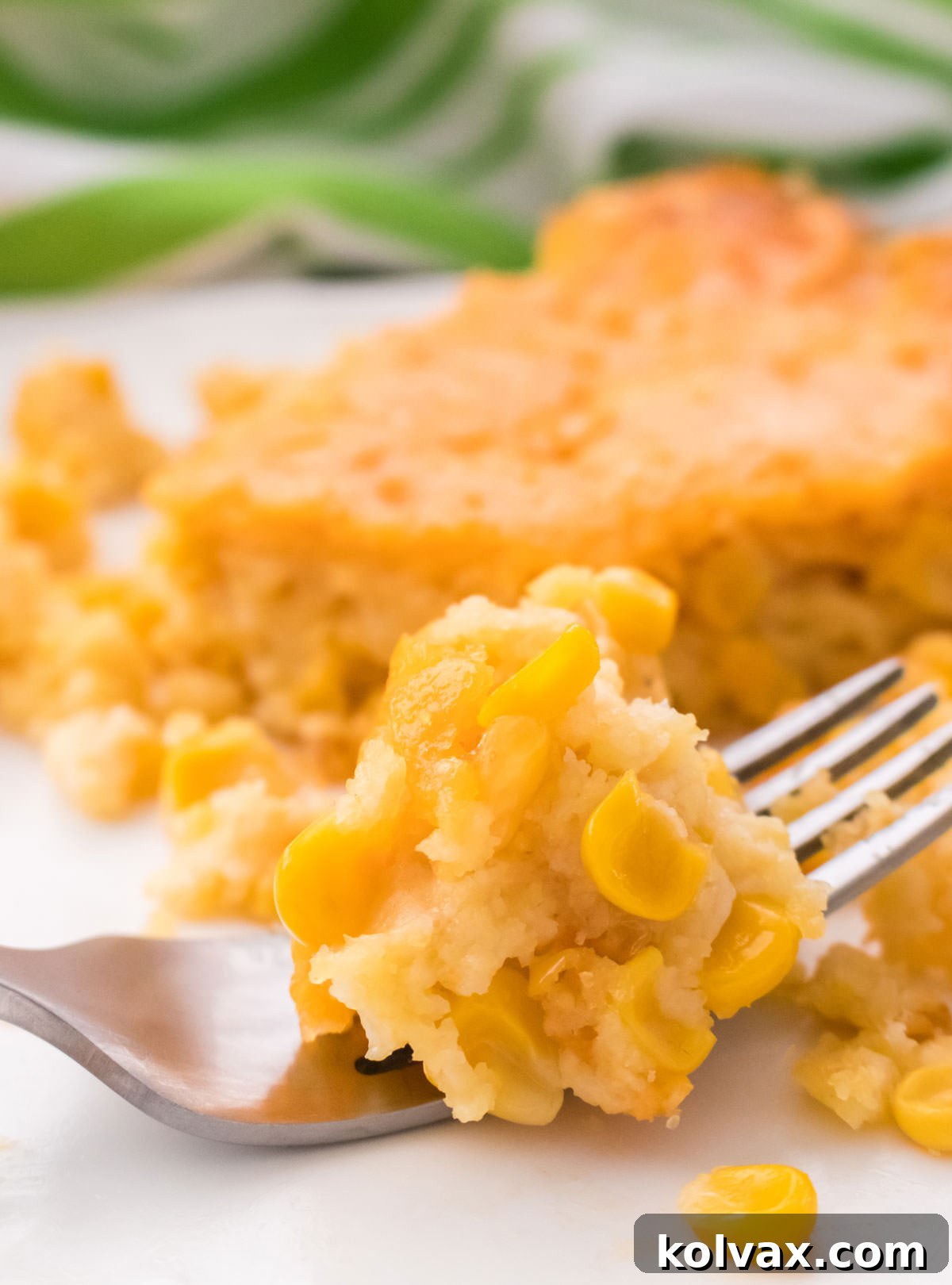 Closeup on a single serving of Corn Casserole on a white dinner plate with a piece resting on a fork, showing its delicious texture.