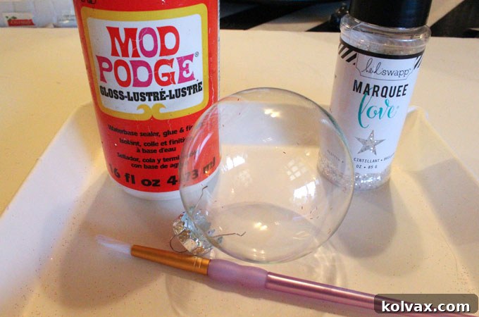 Supplies needed for DIY Glitter Ornaments: glitter, clear ornaments, Mod Podge, and a crafting brush.