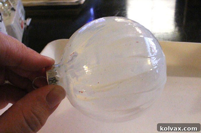 Applying Mod Podge evenly onto a clear Christmas ornament with a crafting brush.