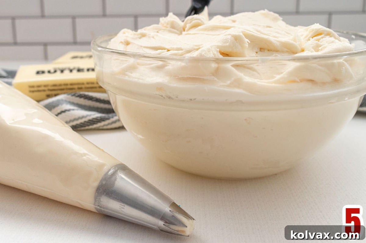 A clear mixing bowl filled with fluffy white buttercream frosting, beside a piping bag also filled with frosting, ready for cookie assembly.