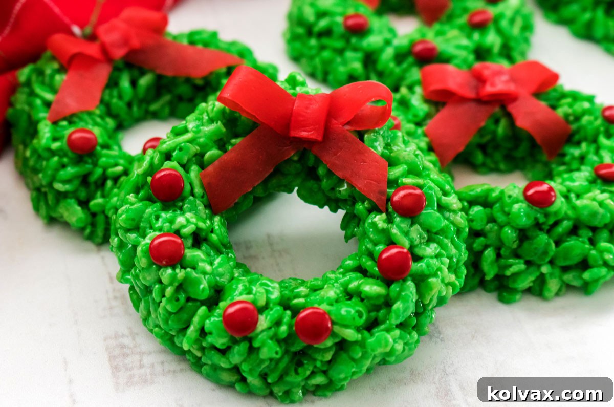 Close-up of four festive Christmas Wreath Rice Krispie Treats arranged on a white surface, showcasing their vibrant green color, red candy embellishments, and edible bows.