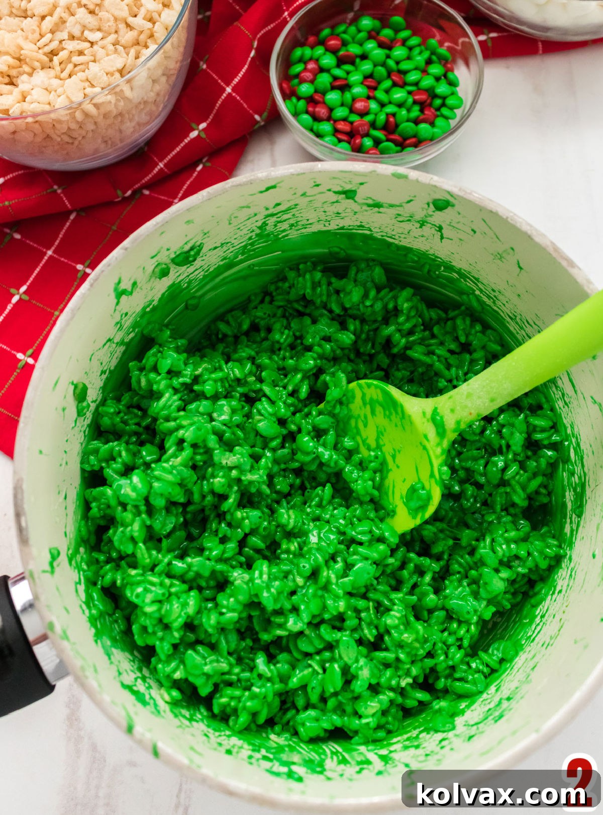 A close-up view of a white pan filled with bright green Rice Krispie Treat mixture, sitting on a white table, ready for shaping.