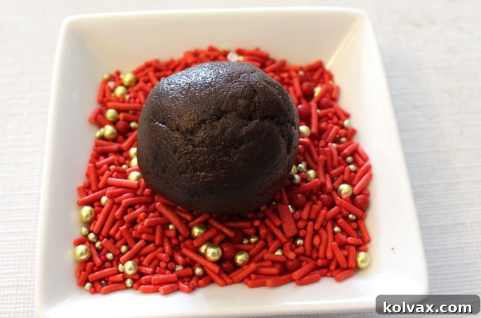 Carefully rolling soft chocolate cookie dough into a bed of vibrant holiday sprinkles.