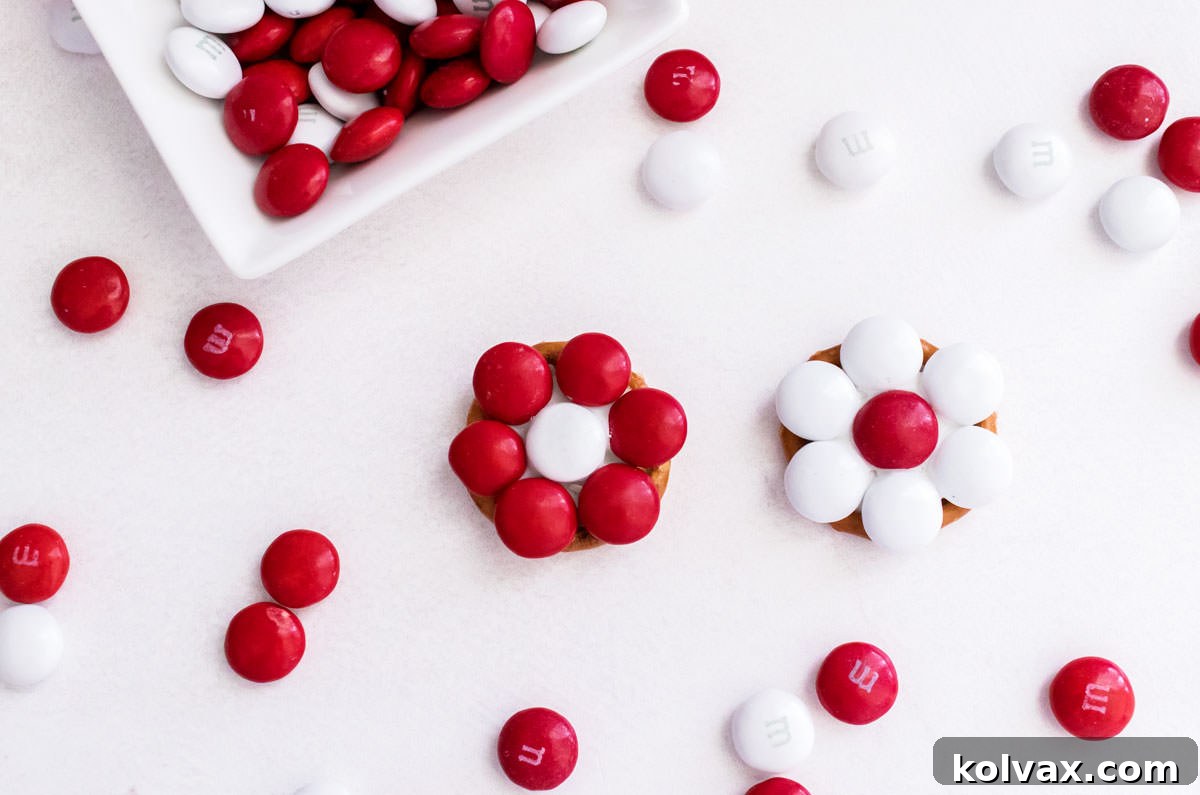 Two Holiday Poinsettia Flower Pretzel Bites laying on a white table surrounded by Red and White M&M's.