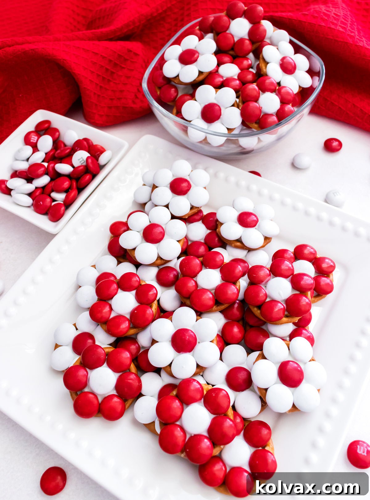 A batch of Holiday Poinsettia Pretzel Bites arranged for a party on a white table with a red kitchen towel.