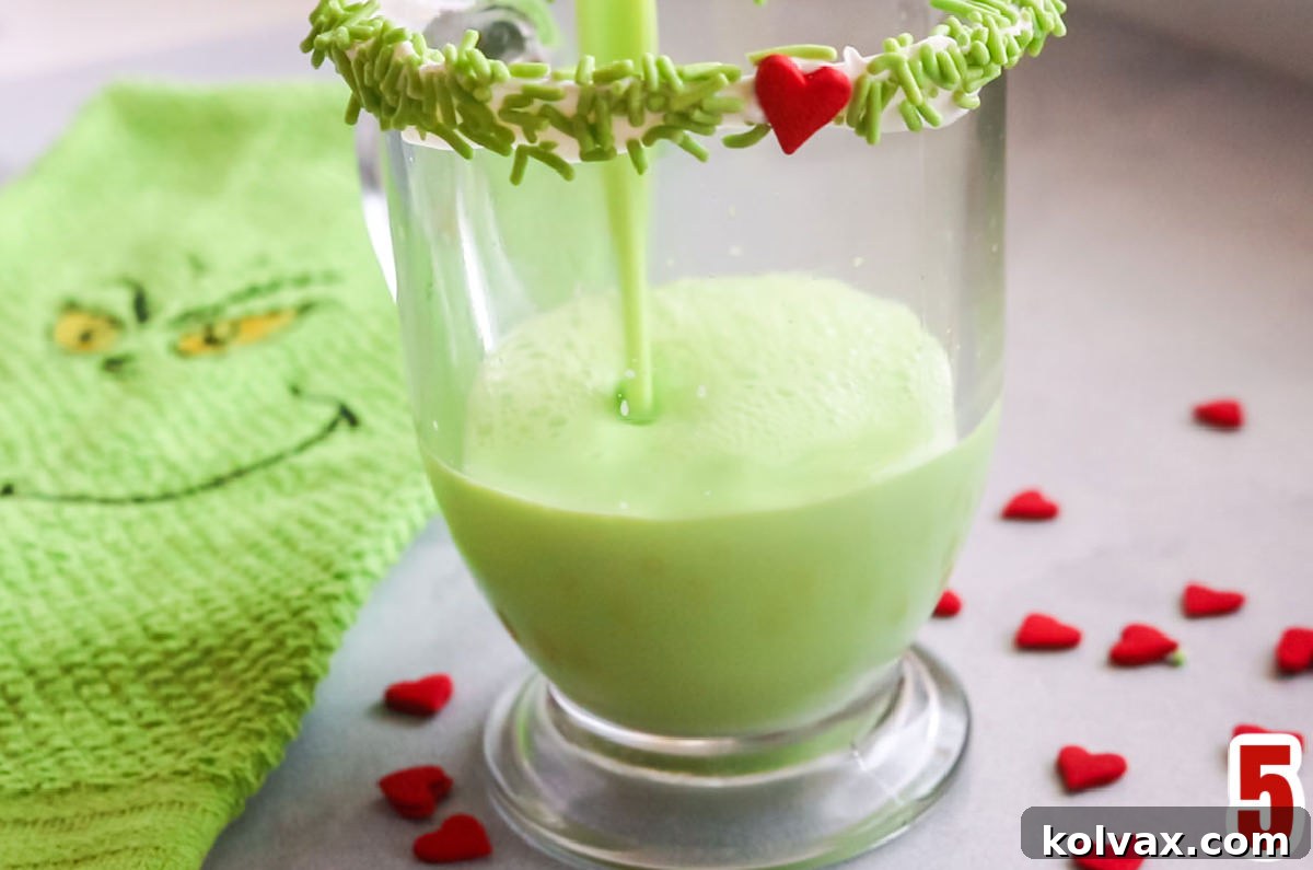Close-up shot of a glass coffee mug being filled with vibrant green Grinch Hot Vanilla Milk, showing the steam rising from the warm beverage, promising a comforting holiday treat.