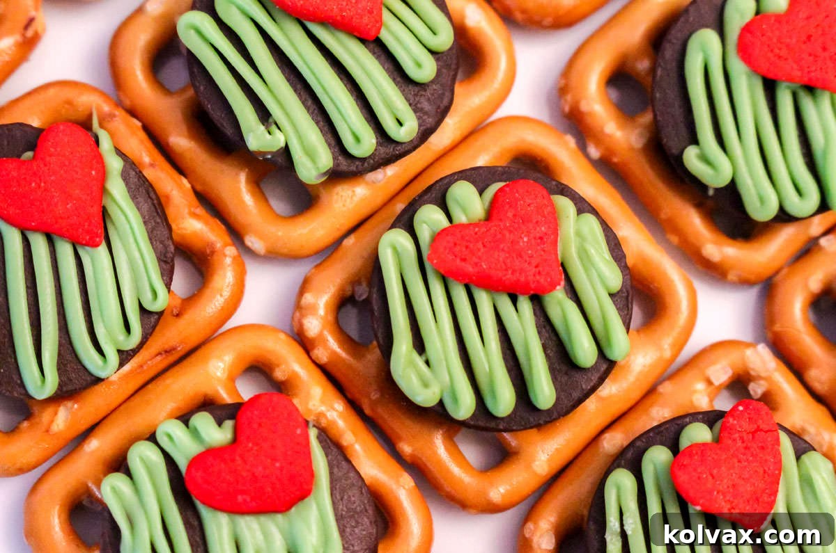 Closeup of a group of Grinch Pretzel Bites aligned on a white table in diagonal rows, showcasing the vibrant green and red heart design.