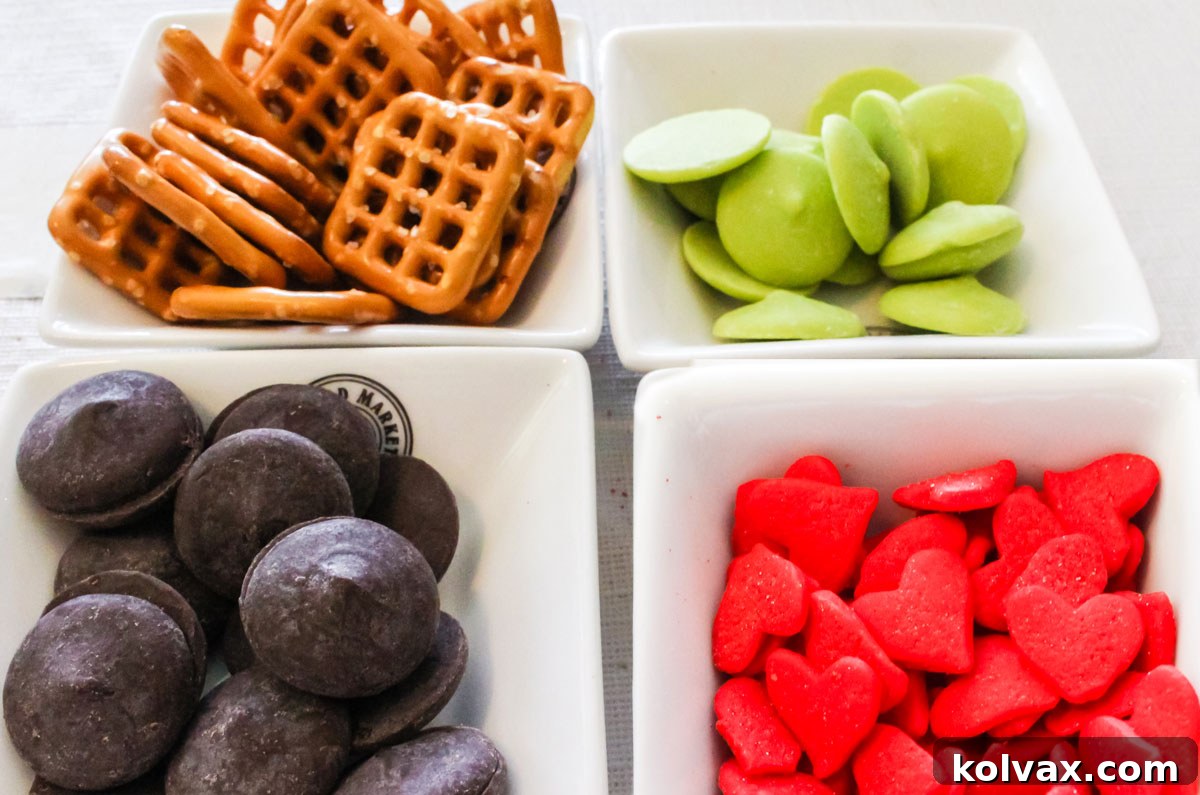 All the ingredients you will need to make Grinch Pretzel Bites including pretzel snaps, Green Candy Melts, Chocolate Melting Wafers and Red Heart sprinkles, neatly arranged.