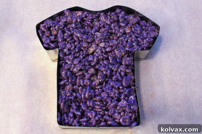 Molding the purple Rice Krispie Treat mixture directly into a football jersey cookie cutter to achieve the desired team shape.