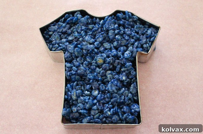 Molding blue Rice Krispie Treat mixture into a football jersey cookie cutter.