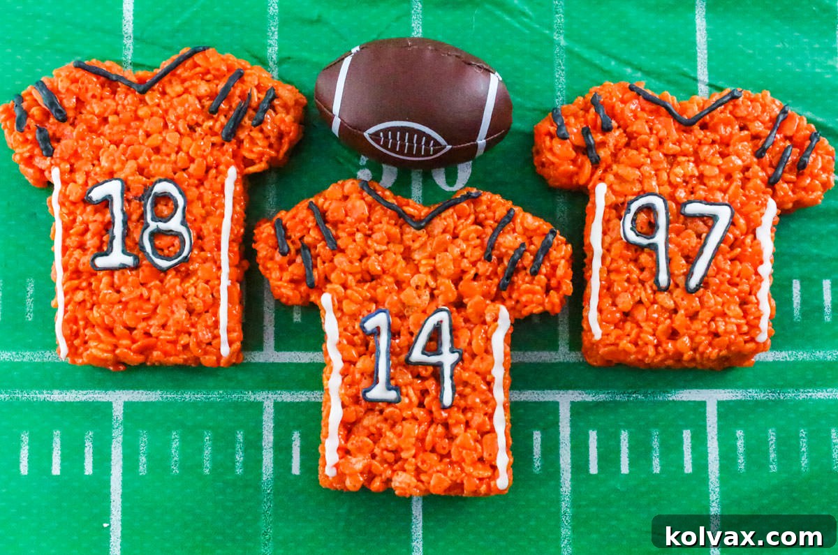 Three Cincinnati Bengals Rice Krispie Treats laying on a table covered with a football party table cloth and a toy football.
