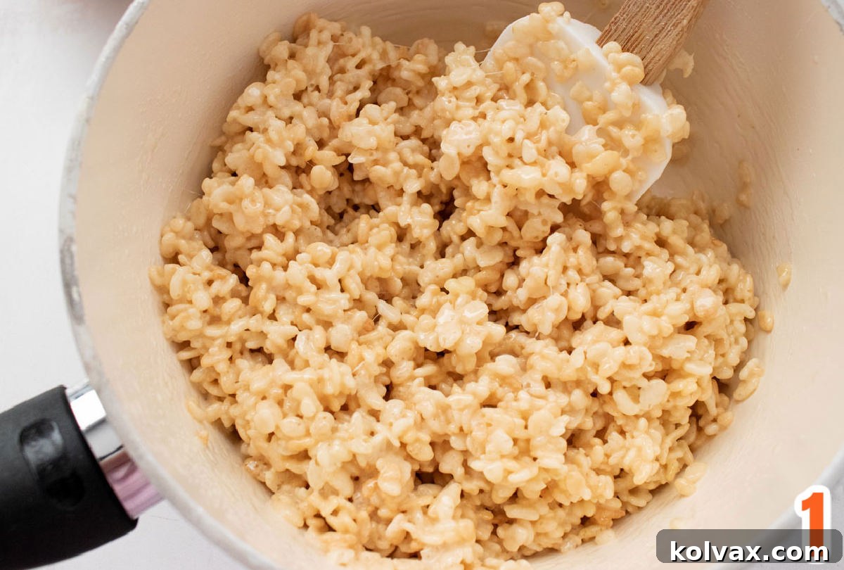 Closeup on a white sauce pan filled with warm Rice Krispie Treat mixture and a wooden spatula.