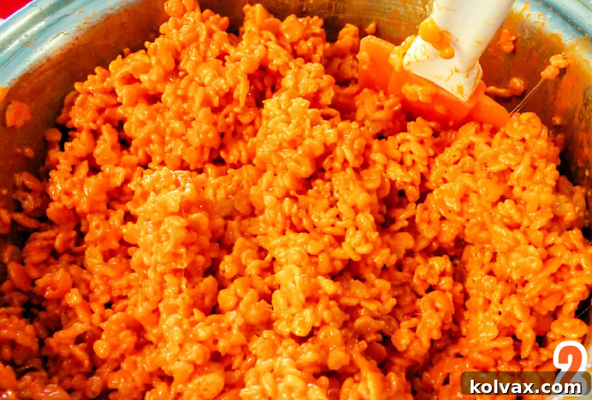 Closeup on a silver sauce pan filled with Orange Rice Krispie Treat mixture and a white spatula.