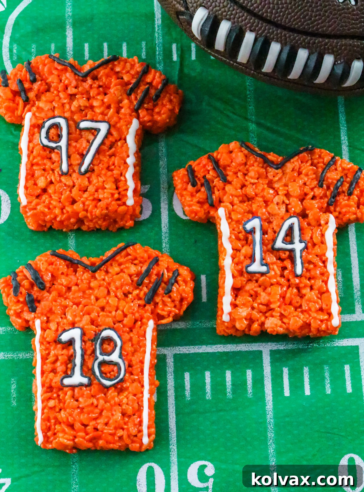 Closeup on three Cincinnati Bengals Rice Krispie Treats laying on a football tablecloth next to a toy football.