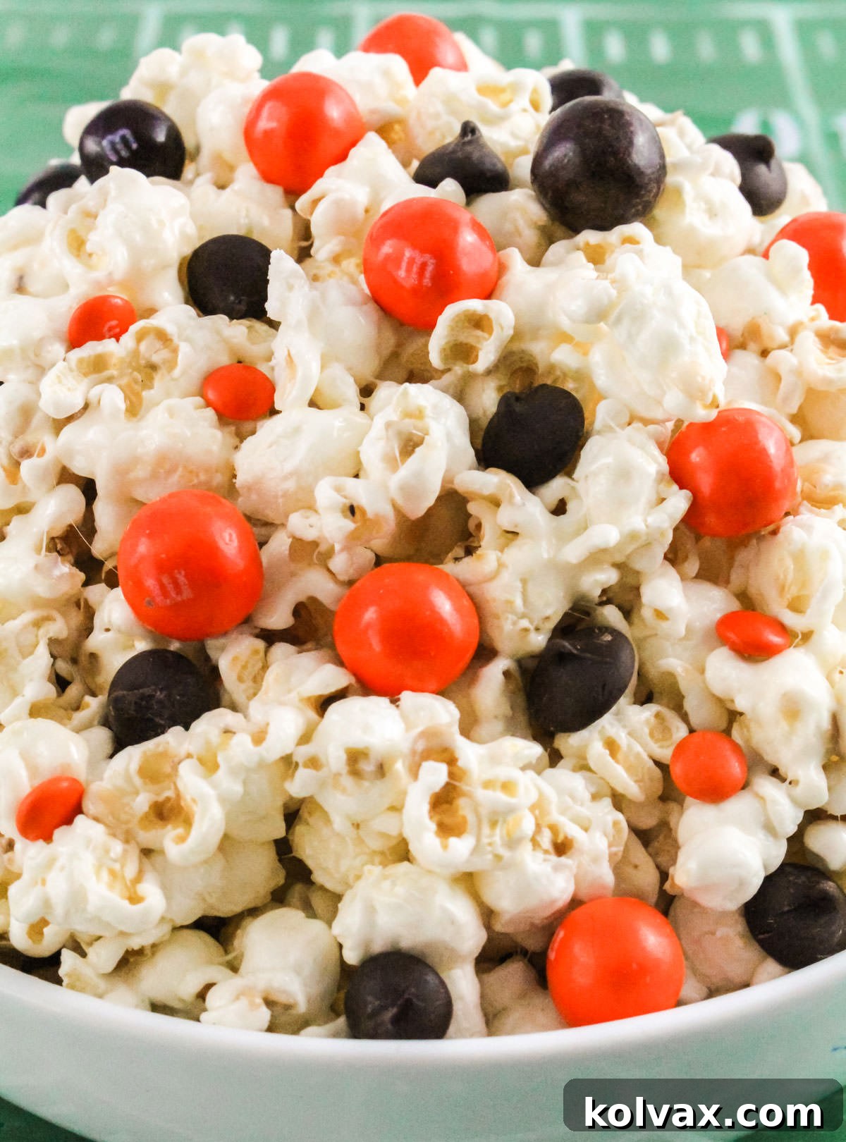 Who Dey Popcorn 9 A large white bowl overflowing with colorful Cincinnati Bengals Popcorn, sitting on a detailed football field tablecloth, ready for a party.