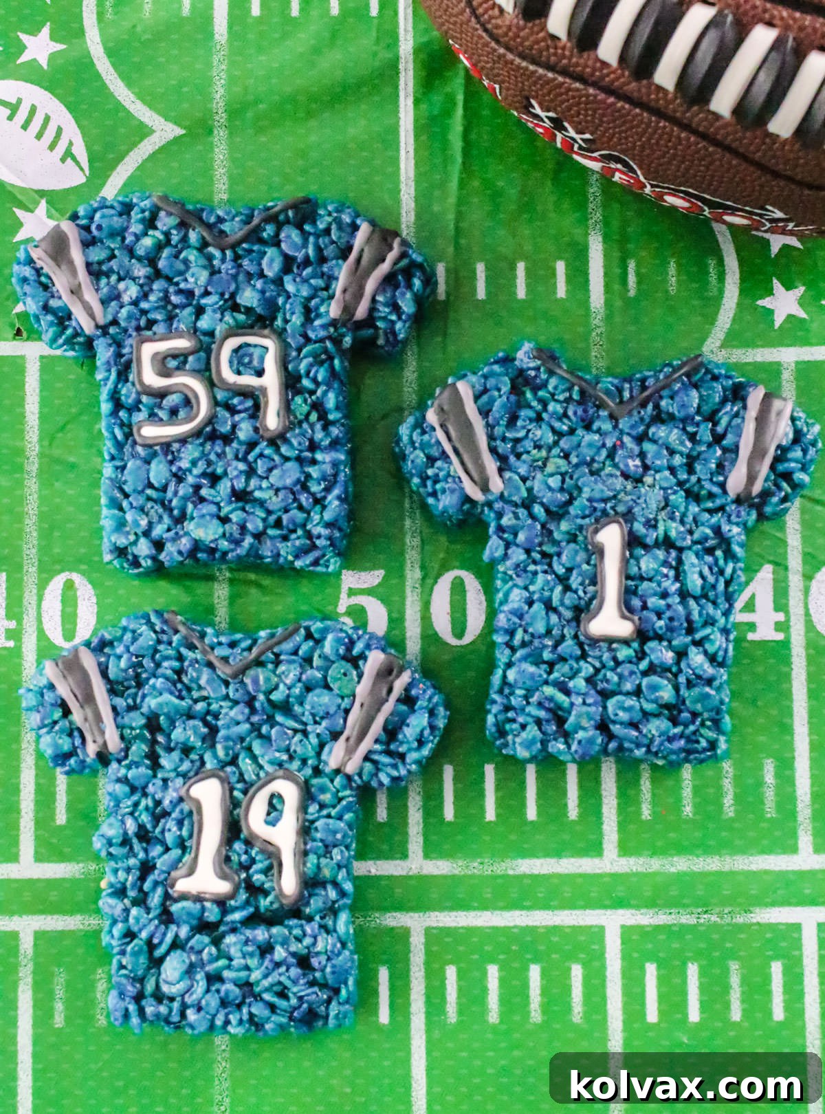 Three perfectly crafted Carolina Panthers Rice Krispie Treat jerseys displayed on a football field themed tablecloth.