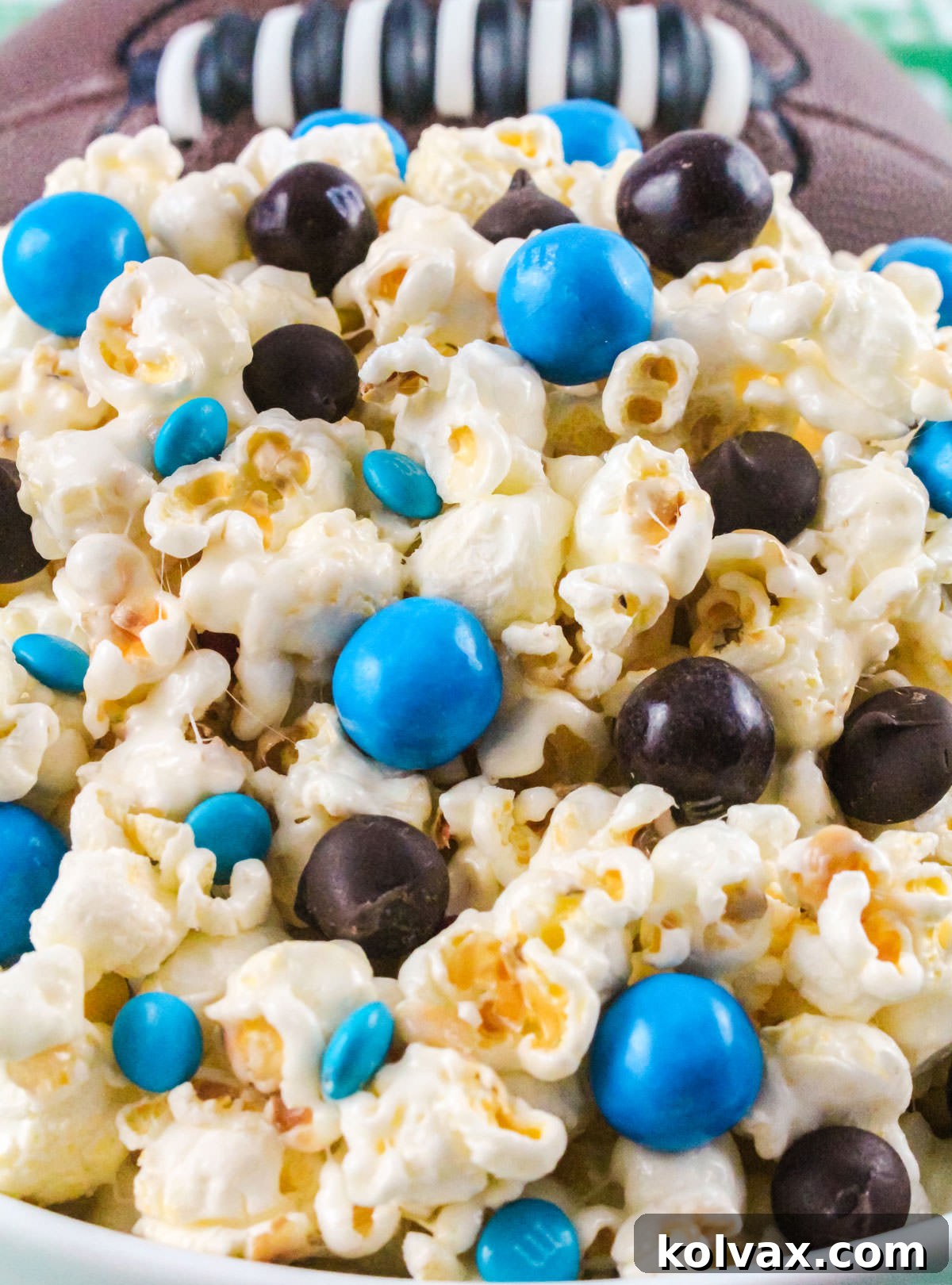 A white serving bowl overflowing with a vibrant batch of Carolina Panthers themed sweet and salty popcorn, with football decorations in the background.