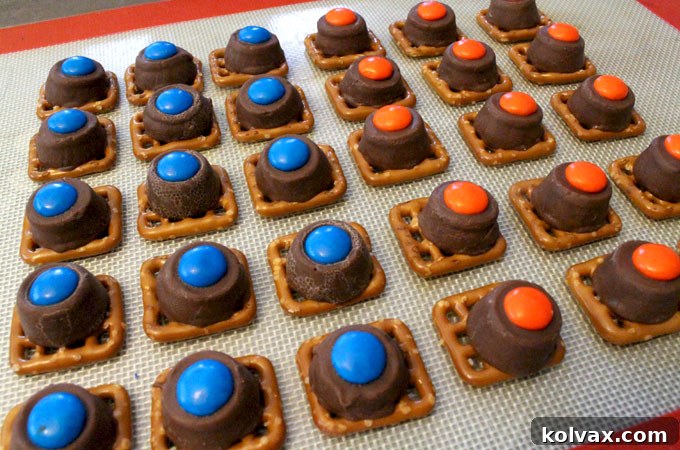 Hand placing an orange M&M onto a warm, melted Rollo candy centered on a pretzel snap