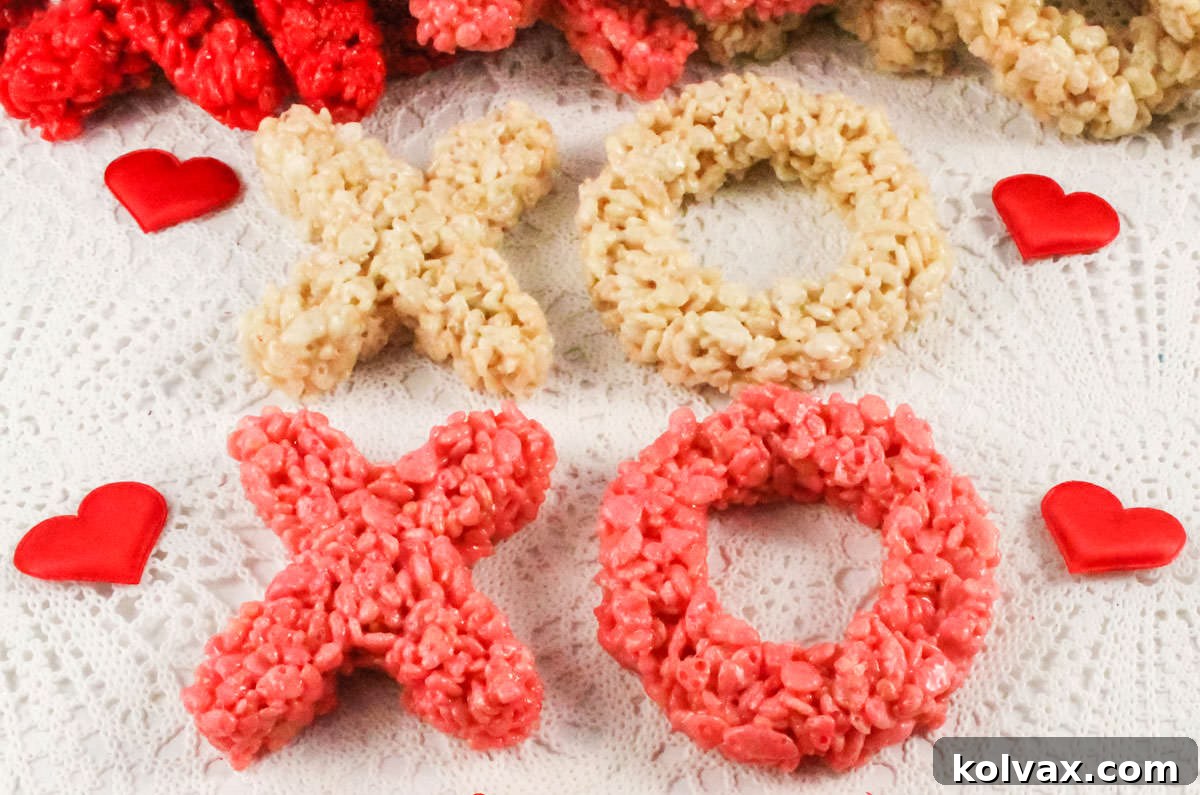 Pink, red, and white X and O shaped Rice Krispie Treats arranged on a white linen, adorned with small red hearts, ready for Valentine's Day.