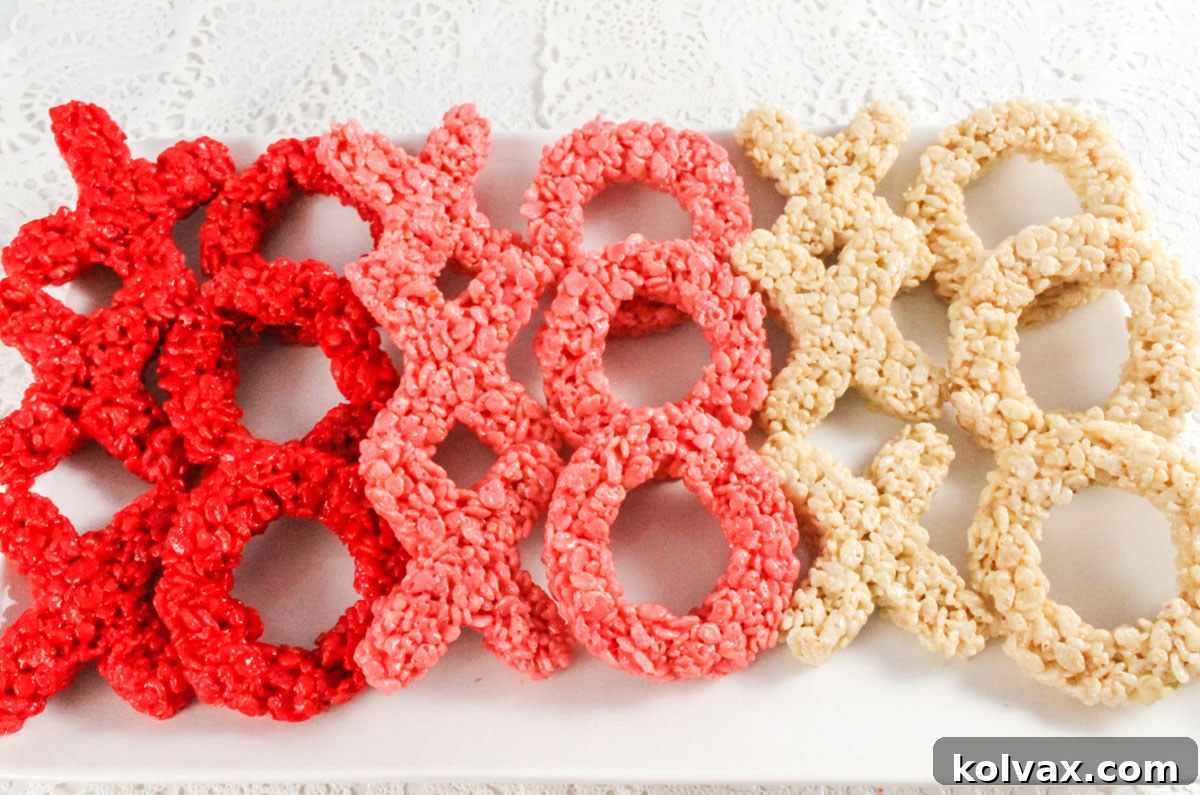 A pristine white serving platter artfully arranged with a colorful assortment of red, pink, and white Hugs and Kisses Rice Krispie Treats.