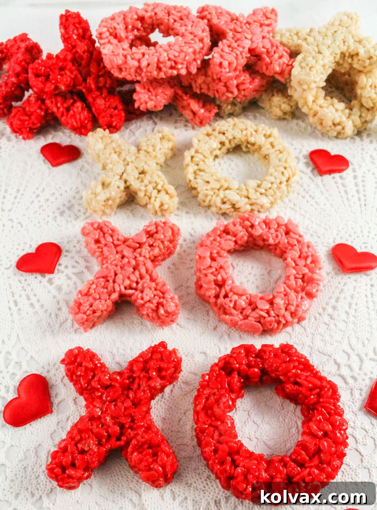 A vibrant display of red, pink, and white X and O shaped Rice Krispie Treats resting on a white linen, surrounded by small decorative red hearts, ready for a Valentine's Day celebration.