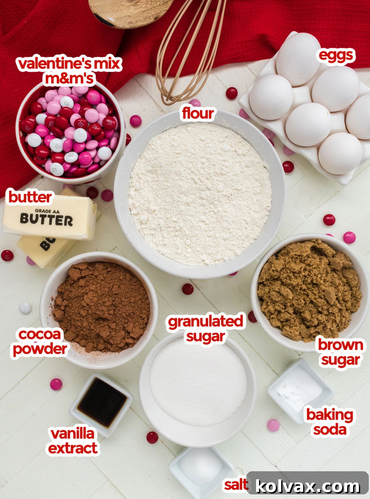 Colorful Valentine M&M Cookies 3 A flat lay photograph showcasing all the ingredients required for Valentine's Day M&M Cookies: a bag of Valentine's mix M&M's, fresh eggs, all-purpose flour, softened butter, unsweetened cocoa powder, granulated sugar, packed brown sugar, vanilla extract, baking soda, and a pinch of salt.