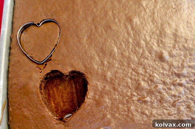 Cutting heart-shaped mini cakes from a baked chocolate sheet cake.