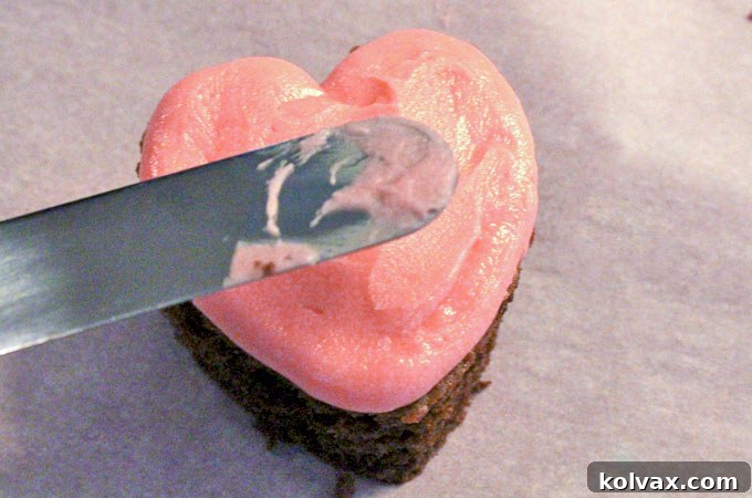 Applying a smooth layer of pink buttercream frosting to chocolate heart cake bites.
