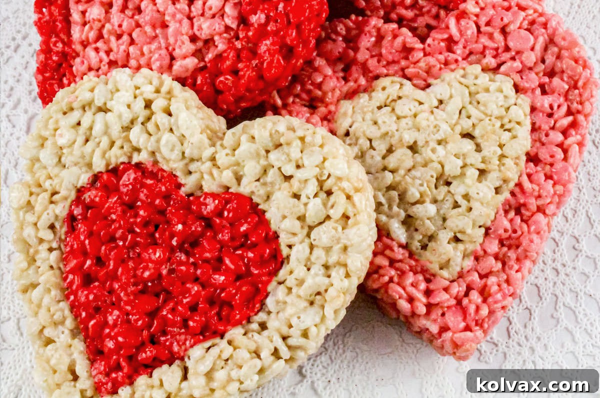 Vibrant red, white, and pink heart-shaped Rice Krispie Treats arranged beautifully on a white lace kitchen linen, ready for Valentine's Day celebrations. The treats feature charming contrasting centers.