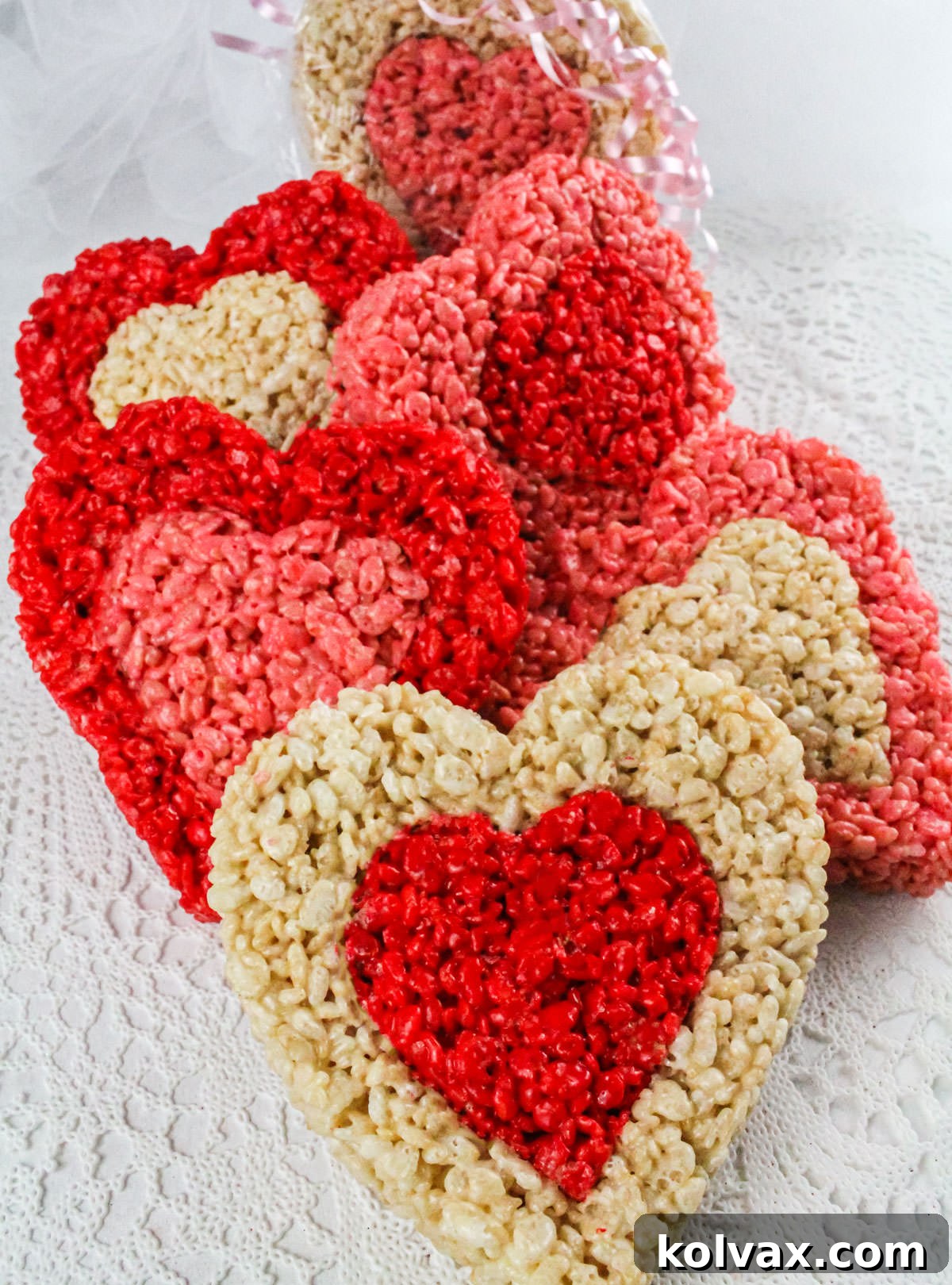 A beautiful stack of red, white, and pink heart-shaped Rice Krispie Treats, each with a contrasting center, artfully arranged on a pristine white lace linen, showcasing their intricate and charming layered design.