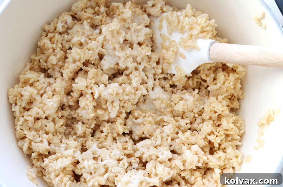 White sauce pan filled with Rice Krispie Treat mixture along with a wood spatula.