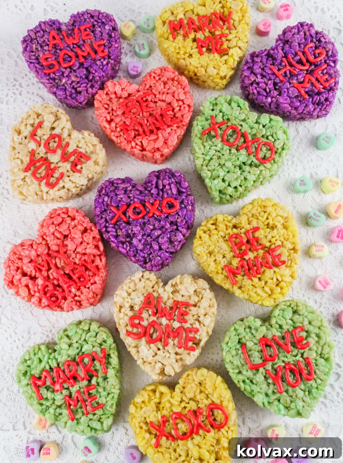 A large grouping of Conversation Hearts Rice Krispie Treats laying on a lace linen surrounded by Conversation Heart candies.