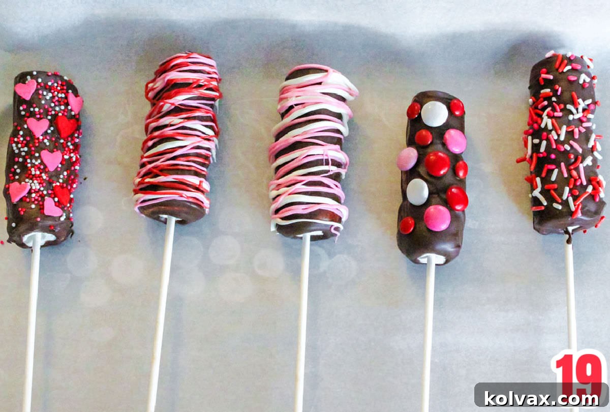 Close up of decorated Marshmallow Wands drying and hardening on a parchment paper covered cookie sheet, showing the various sprinkles and M&M's.