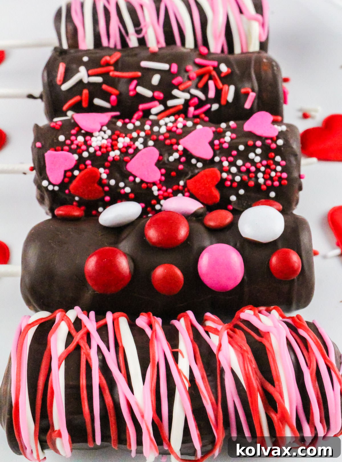 Five Valentine's Day Marshmallow Wands on a white serving platter, decorated in Valentine's M&M's, sprinkles and candy, ready to be served.