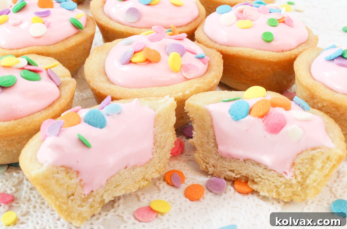 Closeup on a batch of Pink Lemonade Cookie Cups laying on a white table, the cookie cup in the front is cut in half, revealing the creamy pink filling.