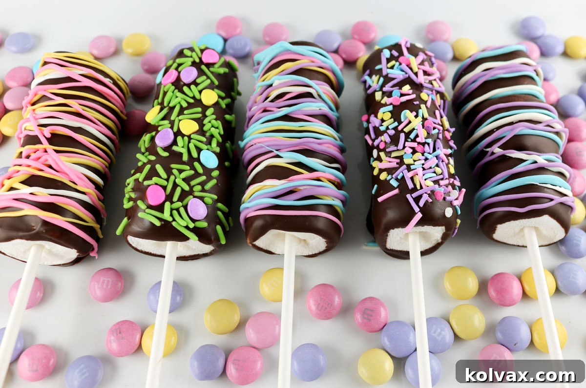 Five colorful Springtime Marshmallow Pops laying on a white surface surrounded by Easter M&M's.