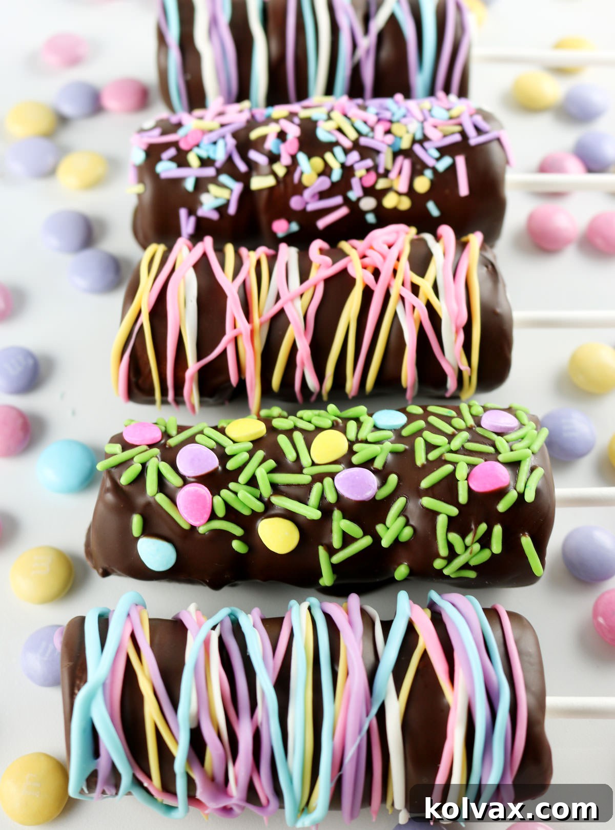 Closeup on six Springtime Marshmallow Pops laying on a white surface surrounded by M&Ms.