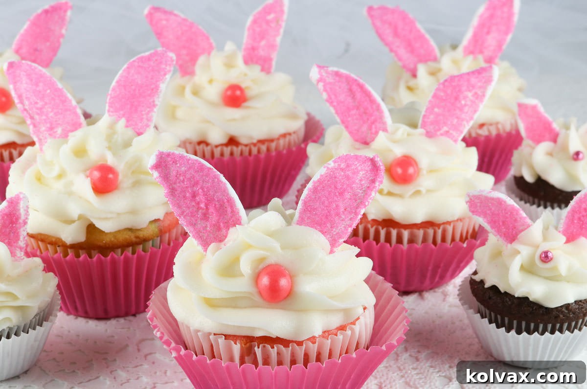 Close up on a batch of regular sized and mini Bunny Cupcakes sitting on a white surface, showcasing their adorable marshmallow ears and pink noses.