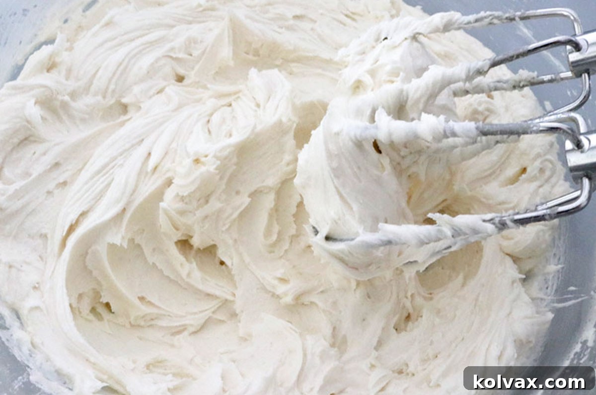 A batch of The Best Buttercream Frosting in a clear bowl with a mixer covered in frosting, showing its smooth, creamy texture.