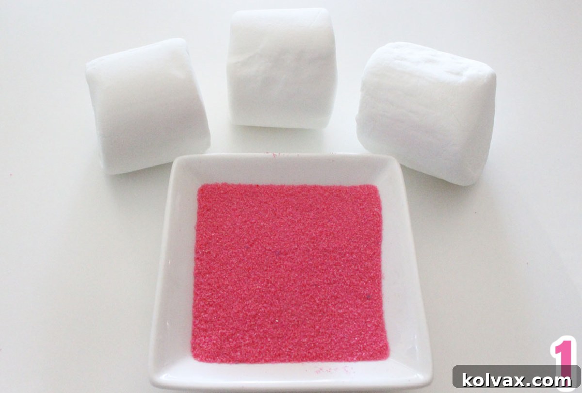 Close up on three Jumbo Marshmallows sitting next to a small white ramekin filled with Pink Colored Sugar, ready for making bunny ears.