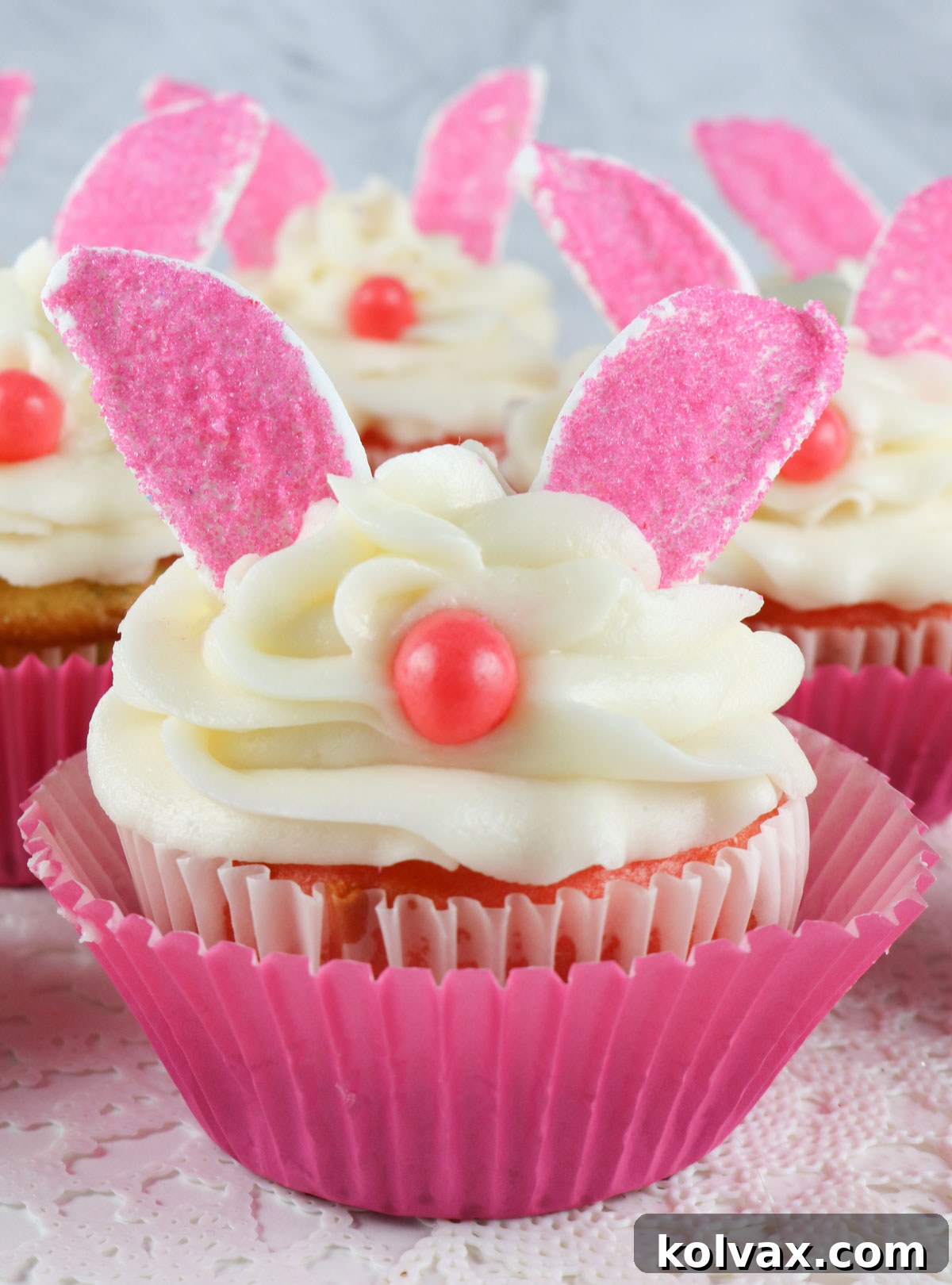 Close up of a Bunny Cupcake sitting on a white doily in front of other Bunny Cupcakes, arranged beautifully for a spring celebration.