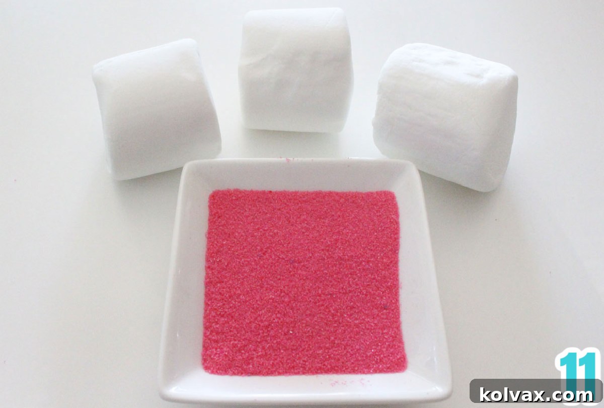 Ingredients for marshmallow bunny ears laid out on a white surface: a bag of jumbo marshmallows and a small glass bowl filled with pink sparkling sugar.