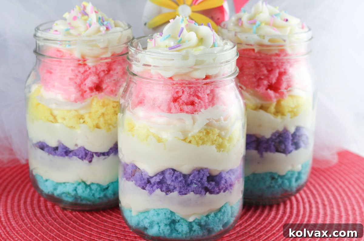 Three colorful Springtime Cupcakes in a Jar, layered with pastel cake and buttercream, sitting on a pink placemat, ready for an Easter celebration.