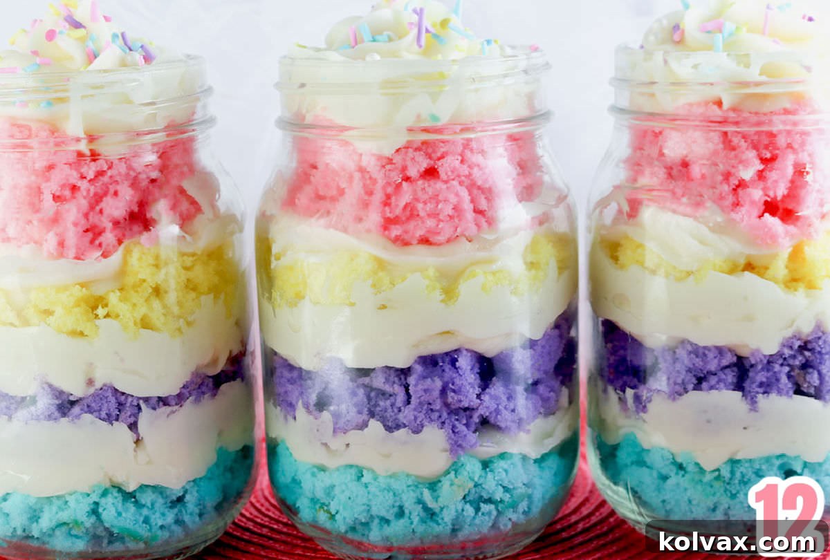 Three beautifully assembled Springtime Cupcakes in a Jar, with colorful layers and frosting swirls, lined up on a pink placemat, showcasing their delightful appearance.