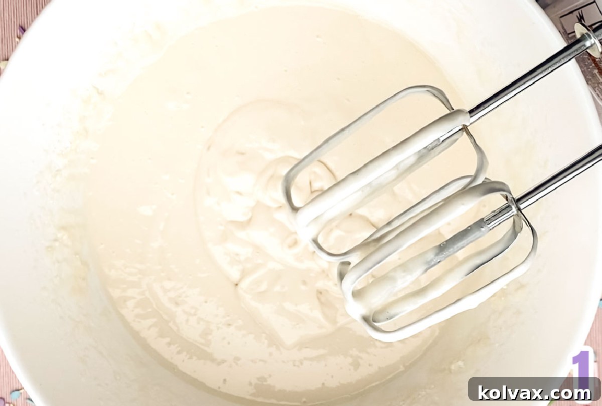 A large white mixing bowl filled with smooth, white cake batter, being mixed with a hand-mixer, ready for coloring.